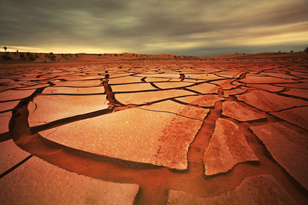 foto de un suelo de tierra seco y agrietado, en el desierto. por encima un cielo de nubes grises y fondo amarillo